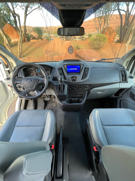 View from an RV rental's front cabin: Ford van dashboard, Alpine screen, and stunning desert landscape outside.
