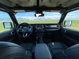 Inside a Jeep Wrangler, showing dashboard and steering wheel, with vast mountains and green fields. Perfect for adventure, like an RV rental trip.