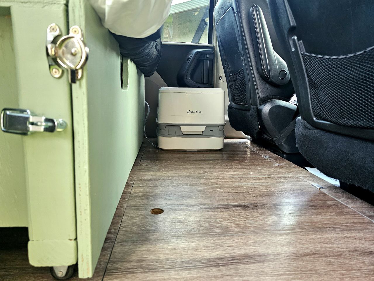Inside an RV rental: a portable toilet sits on wood flooring next to a seat and green cabinet. — photo 12