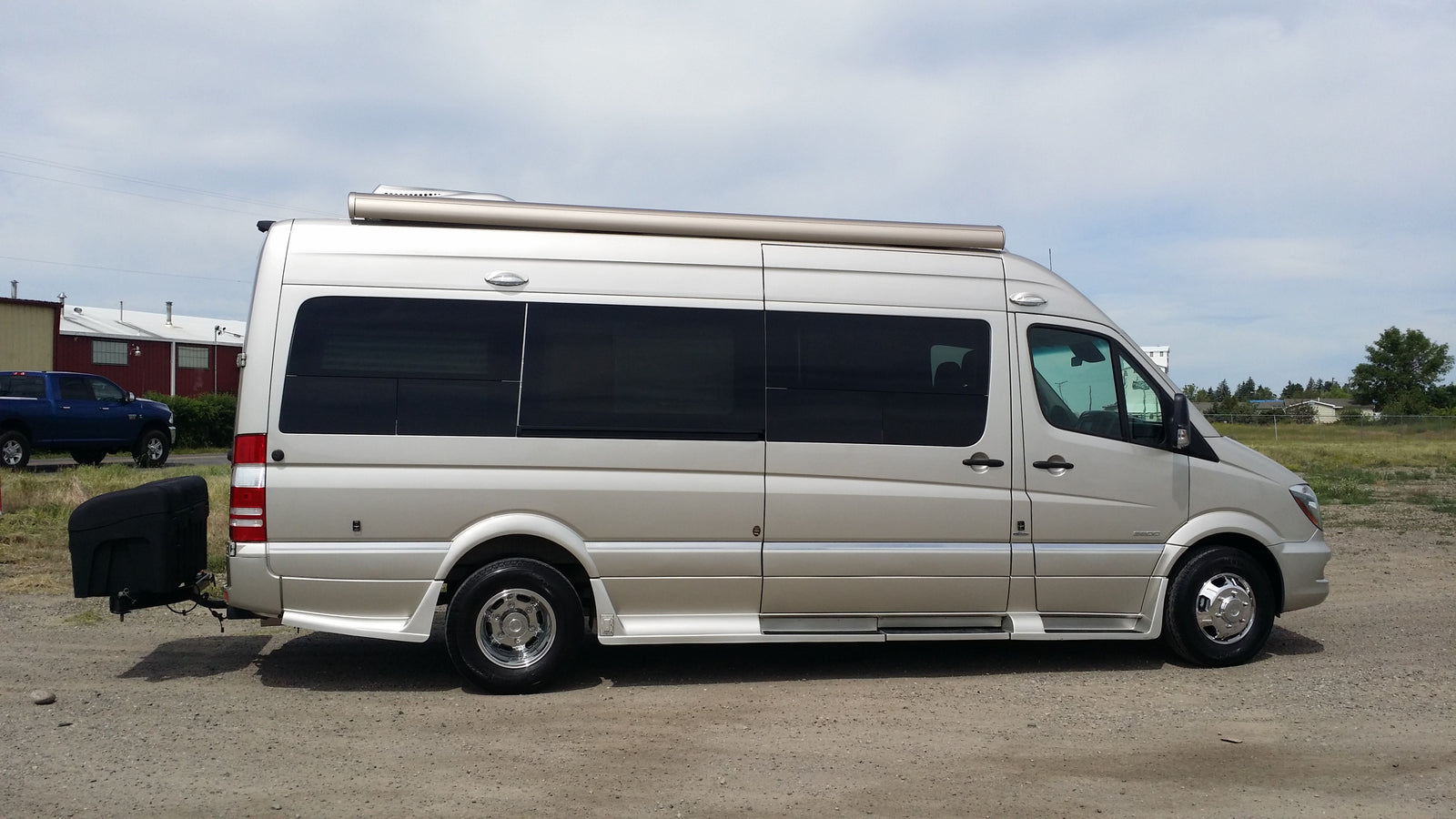 Beige Mercedes-Benz Sprinter RV rental camper van with roof awning, running boards, and rear cargo box.