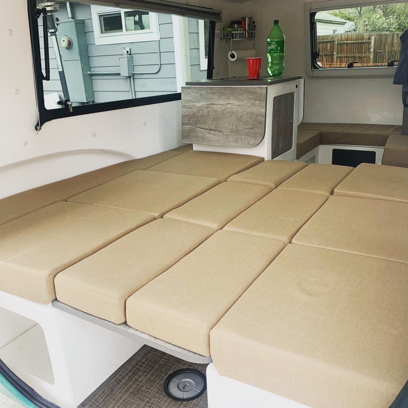 Versatile beige cushioned lounge area/bed in an RV rental, complete with a compact kitchen counter, ideal for travel.