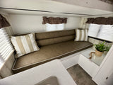 Cozy RV rental interior featuring a brown sofa, striped pillows, window blinds, and compact sink area for comfortable travel.