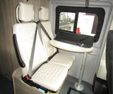RV rental interior: White cushioned seating with seatbelts and a round table inside a camper van.
