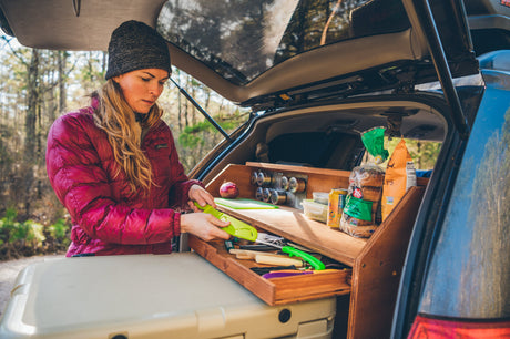 Woman prepares food using a custom portable kitchen in an SUV trunk, ideal for RV rental road trips.