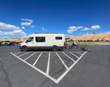 An RV rental camper van parked in a desert lot. A person prepares bikes for outdoor adventure against a scenic backdrop.
