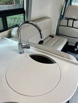 Explore this RV rental's bright interior! Modern kitchenette with white counter, chrome faucet, & integrated sink/cover, plus comfy seats.