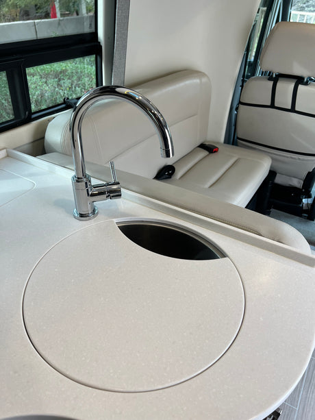 Explore this RV rental's bright interior! Modern kitchenette with white counter, chrome faucet, & integrated sink/cover, plus comfy seats.