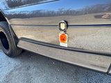 A grey Jay Flight RV rental, awning extended and door open, is perfectly set up in a serene, treed campsite.