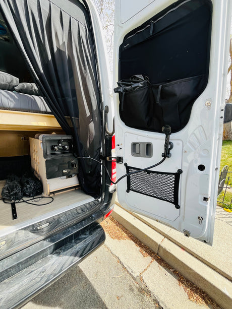 Open back of an RV rental: custom bed, portable sink, and outdoor shower on the door. Ready for your van life adventure.