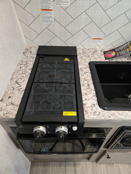 This RV rental kitchen features a gas stove with a glass cover, microwave, and sink, displaying important safety warnings.