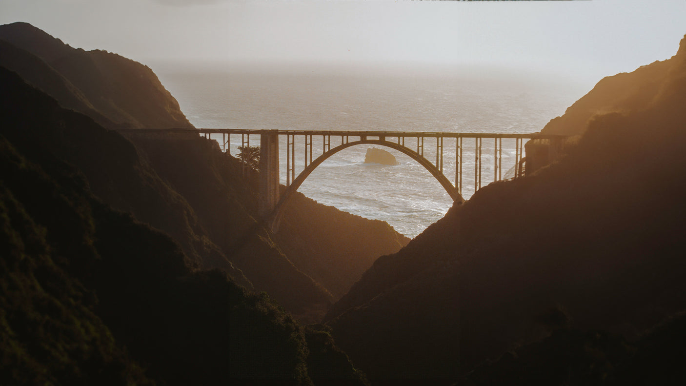 Iconic Bixby Creek Bridge in Big Sur, framed by shadowed cliffs, with sunlit Pacific Ocean views for your RV rental road trip.
