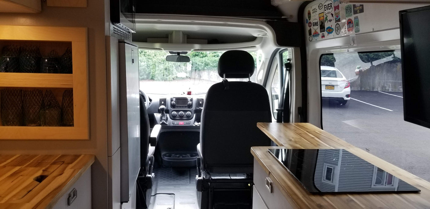 Inside an RV rental, featuring a full kitchen with cooktop, front cabin area with seats and dashboard, plus window view.