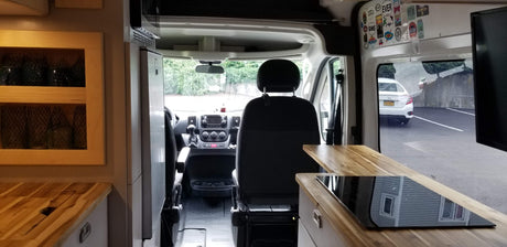 Inside an RV rental, featuring a full kitchen with cooktop, front cabin area with seats and dashboard, plus window view.