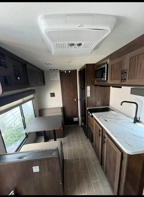Spacious rv rental interior featuring a dinette, full kitchen with microwave, sink, stove, fridge, and overhead AC unit.