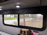 Inside an rv rental: a window with screen reveals a street, house, and trees. Interior features a recessed light, valance, and tan bag.