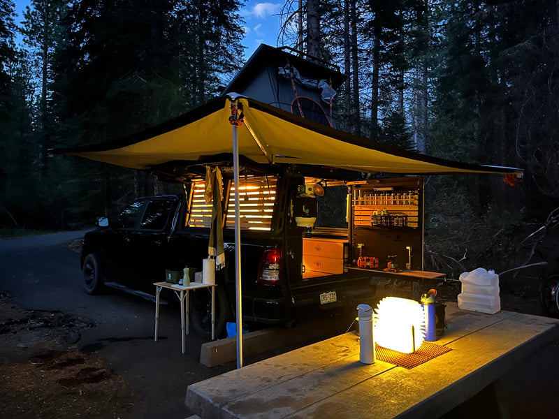 RV rental truck camper setup at night, showcasing a pop-up tent, extended awning, and illuminated mobile kitchen for overlanding. — photo 2