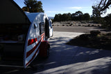 T@G teardrop camper rv rental, rear galley & side door open, parked outdoors in dappled sunlight.