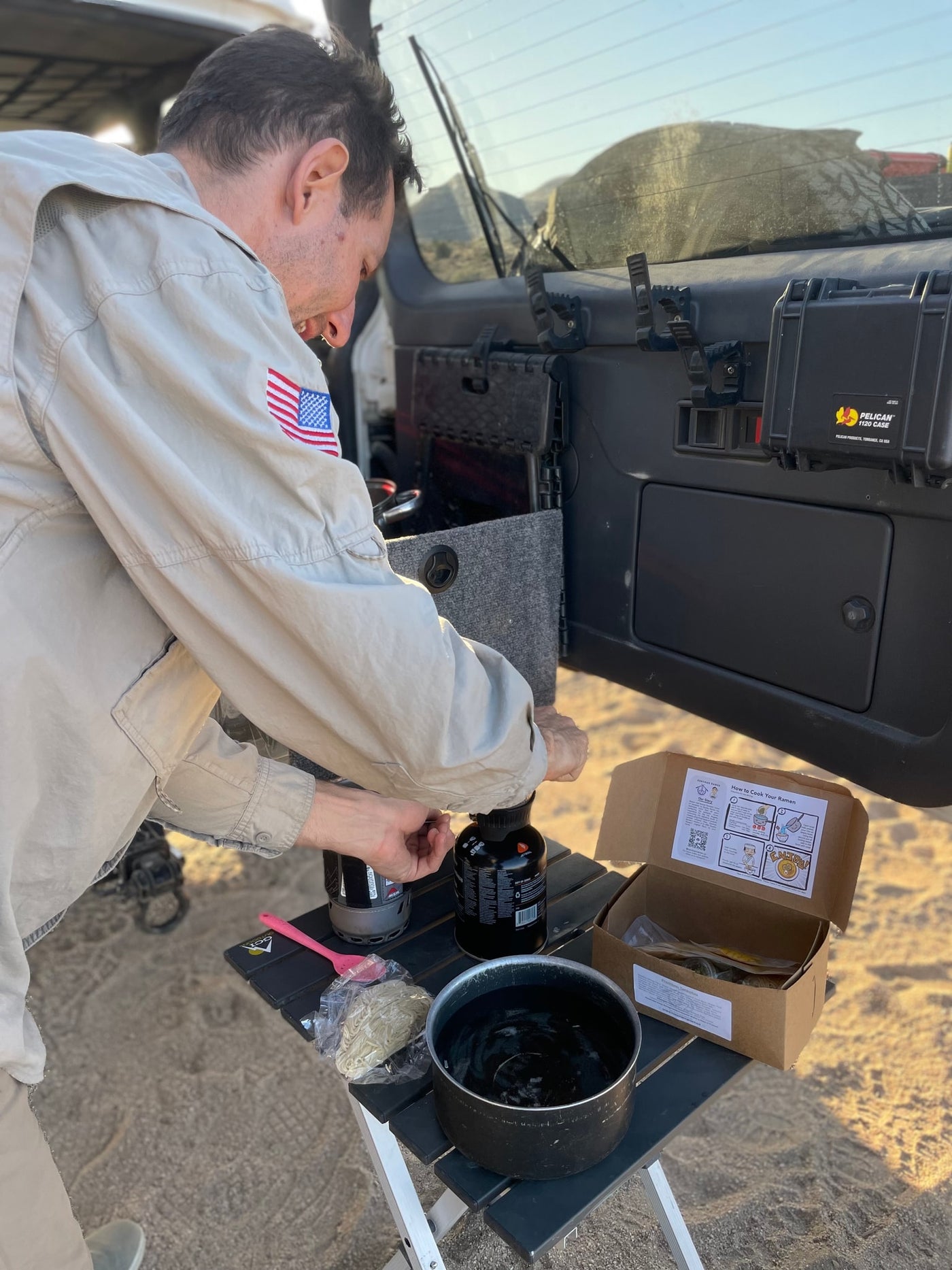 Man prepares ramen on a portable stove at an outdoor camp kitchen, potentially from an rv rental, amidst scenic views. — photo 14