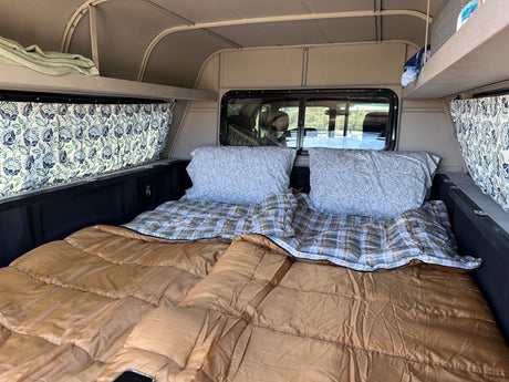 Cozy truck bed camper interior setup with sleeping bags, pillows, and curtains. Perfect for an RV rental adventure.