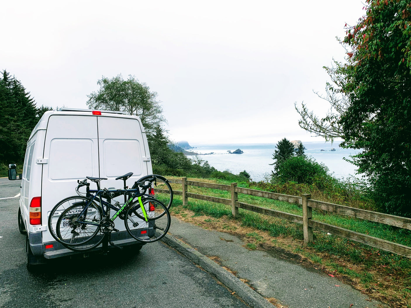 Enjoying a coastal road trip in an RV rental: white camper van with bikes parked overlooking the ocean and rocky coastline.