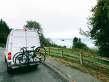 Enjoying a coastal road trip in an RV rental: white camper van with bikes parked overlooking the ocean and rocky coastline.
