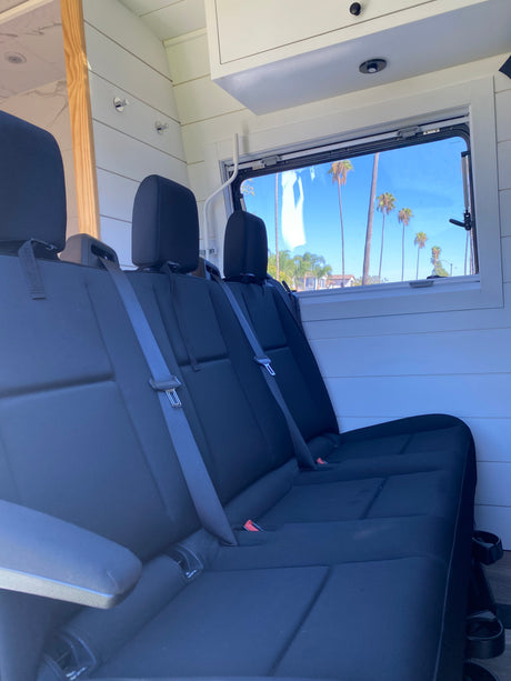 Spacious RV rental interior featuring black passenger seats, white paneling, and a sunny window view with palm trees.