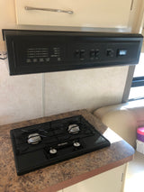 RV rental kitchenette features a Suburban two-burner stove and an overhead control panel with tank levels, battery, and generator controls.