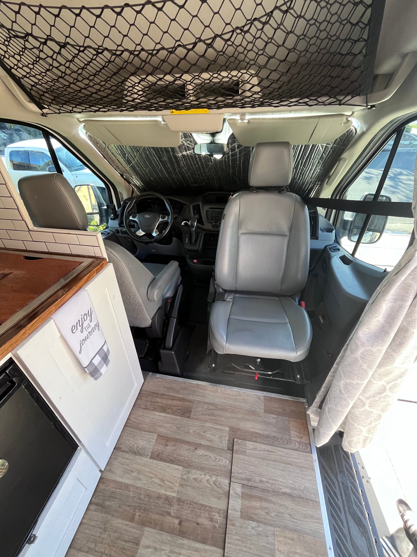 RV rental camper van interior. Front cabin view from living space, showing wood floor, sunshade, and overhead net.