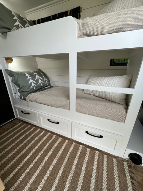 Cozy RV rental bunk beds with built-in storage and neutral decor, featuring a window and striped rug, maximize space for travel.