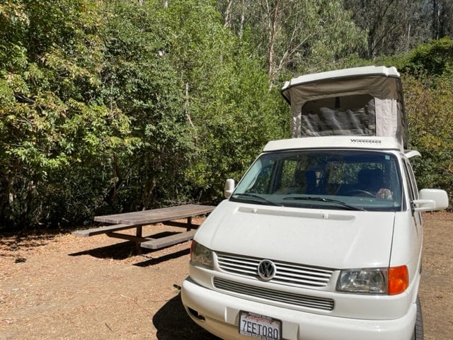  and a window offering a tree view.|Cozy RV rental interior: pop-top camper with kitchen & dining setup — photo 17