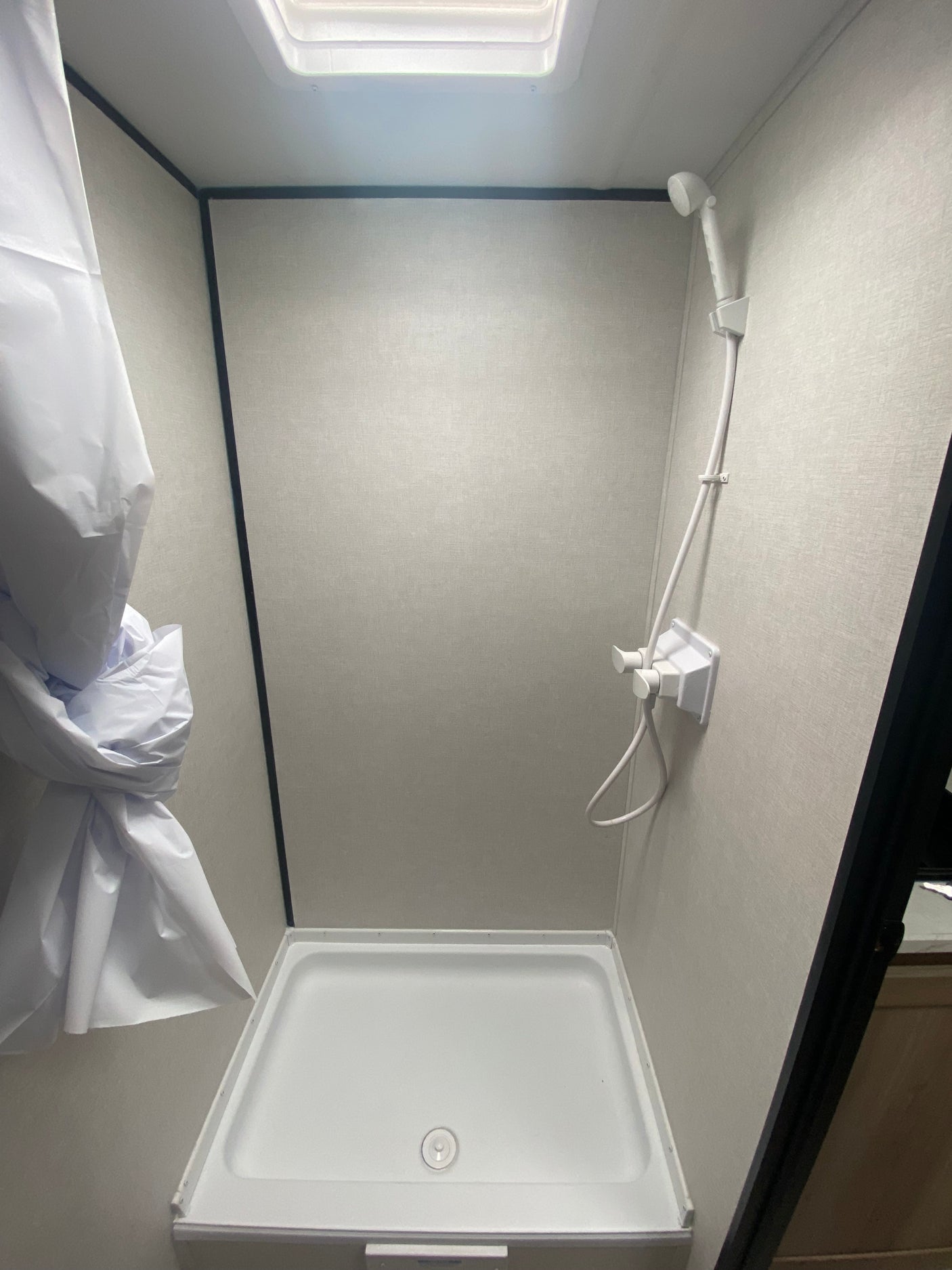 Inside a clean RV rental shower featuring a white shower pan, head, and light walls for comfortable travels.
