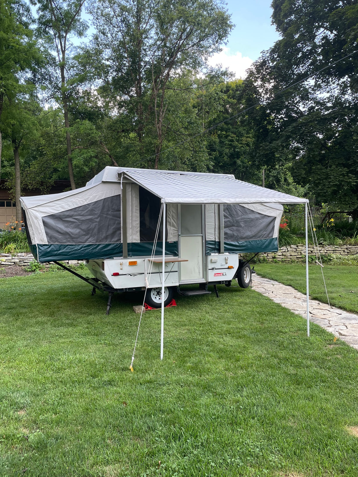 A Coleman pop-up camper is set up on grass with its awning extended