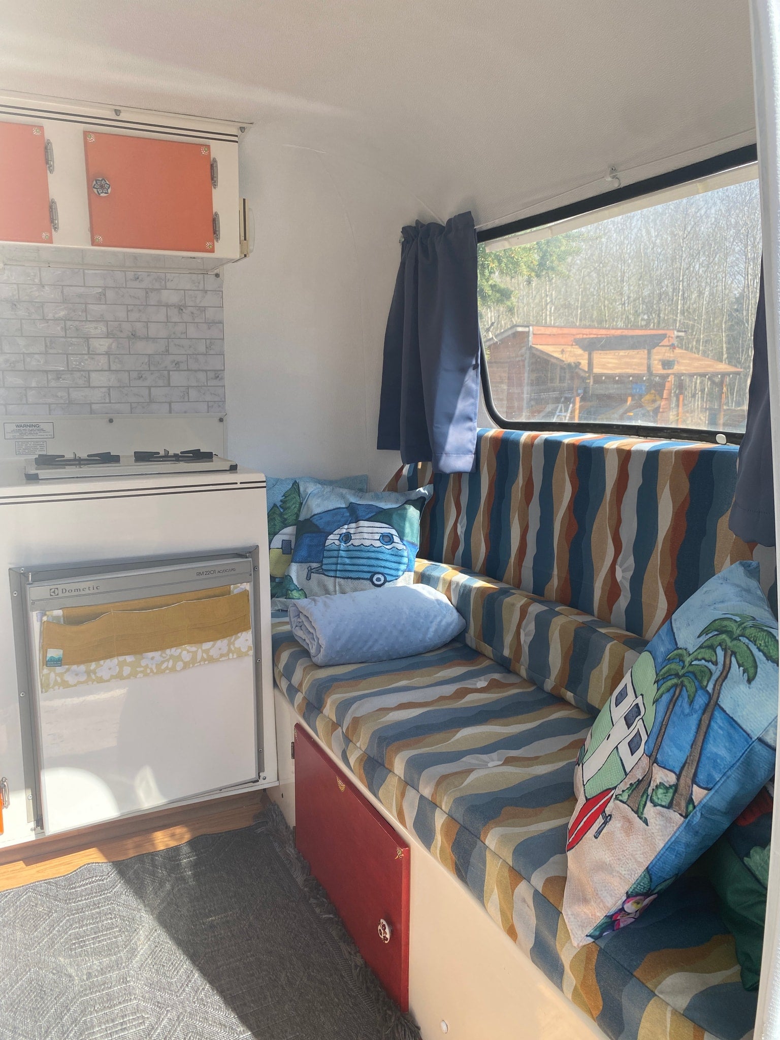 RV rental interior with a compact kitchen, colorful seating, and window view of nature through closed curtains.