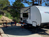 This Yellowstone rv rental provides a complete outdoor setup: extended awning, cooking station, and chairs by a scenic river campsite.
