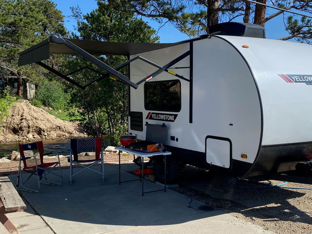 This Yellowstone rv rental provides a complete outdoor setup: extended awning, cooking station, and chairs by a scenic river campsite.