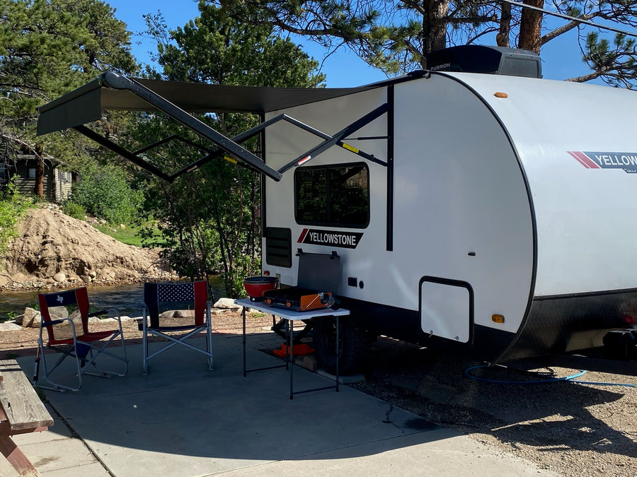 This Yellowstone rv rental provides a complete outdoor setup: extended awning, cooking station, and chairs by a scenic river campsite.