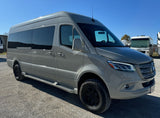 A sleek grey Mercedes-Benz Sprinter van, ready for rv rental, parked outdoors on gravel. Other RVs are in the background.