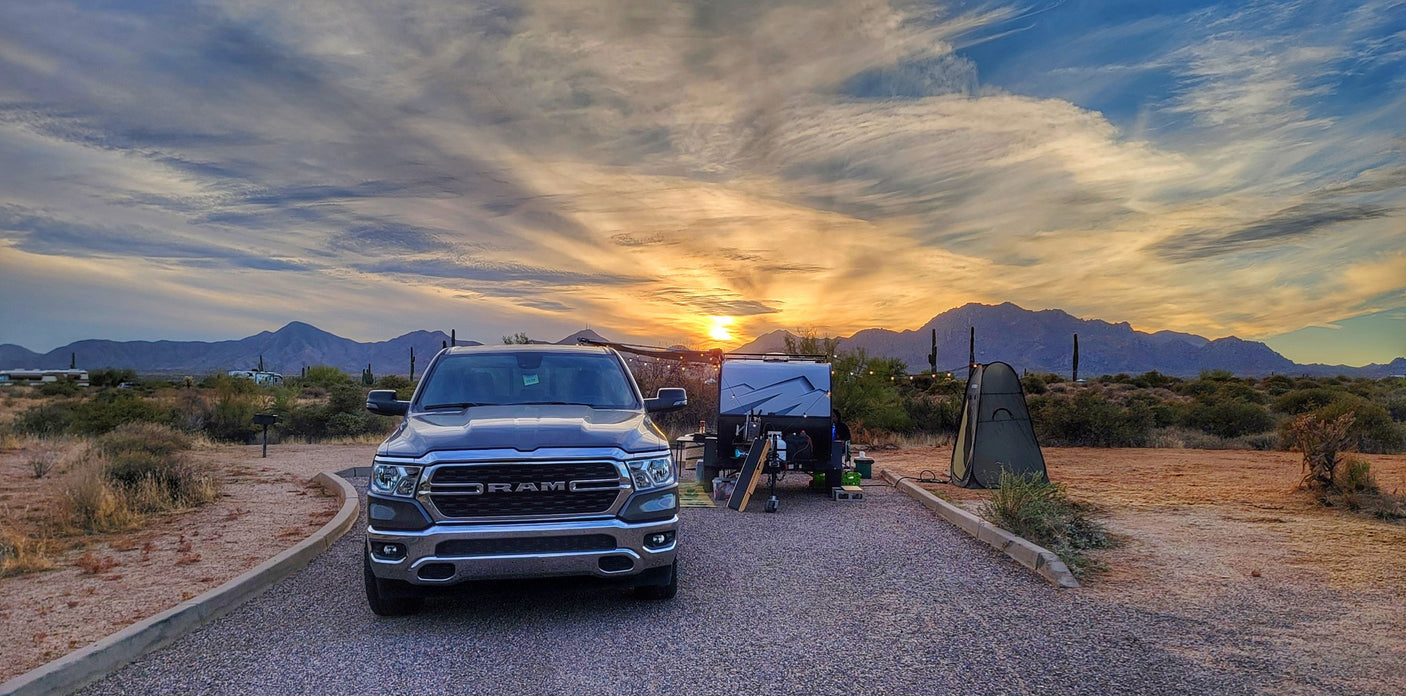 Desert RV rental camping: truck, trailer, & tent at sunset with mountains. Enjoy the vibrant sky!