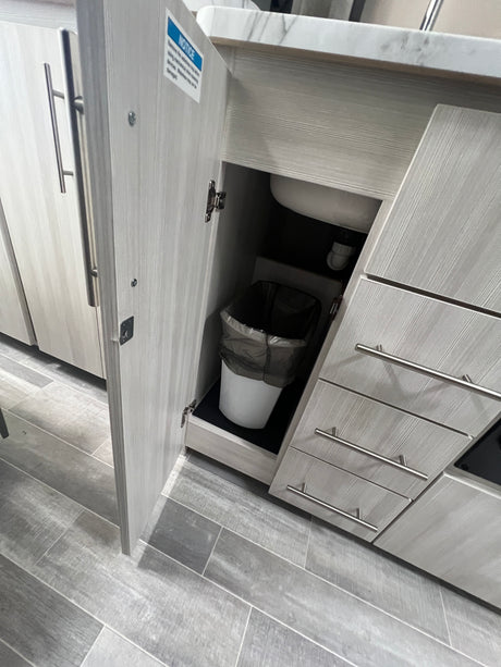 Efficient **RV rental** kitchen with under-sink trash, drawers & light wood cabinets on a tiled floor.