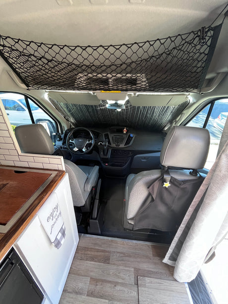 Inside this RV rental camper van: a neat cockpit with sunshade, overhead net, and a compact kitchen. Ready for adventure!