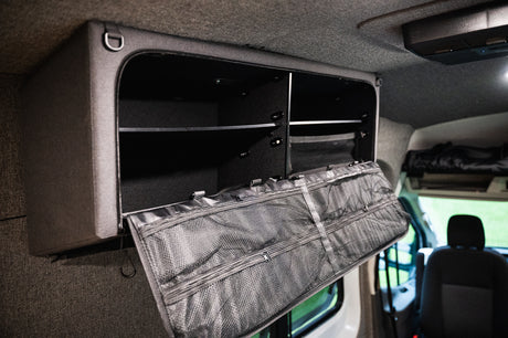 Overhead fabric storage with a soft mesh door, open to reveal shelves and pockets for organization in an RV rental.