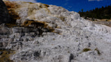 Discover Yellowstone's colorful Mammoth Hot Springs on an rv rental trip. White, orange & brown terraced formations under a blue sky.