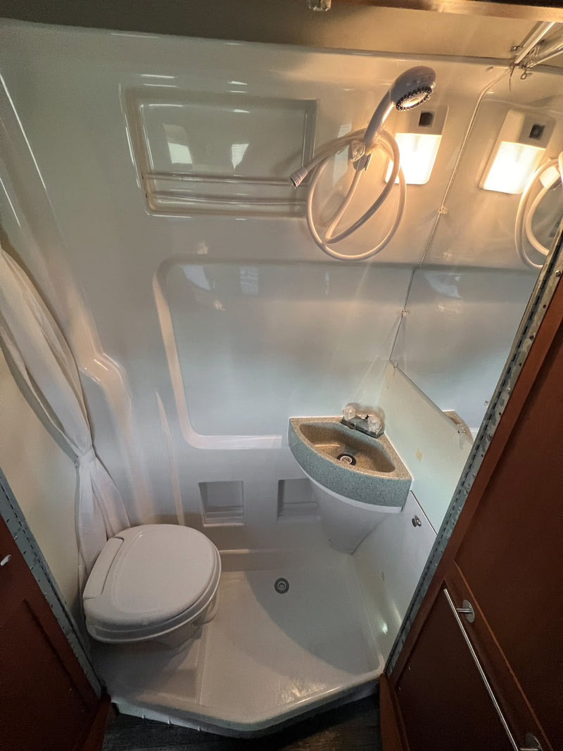 Inside an RV rental: a compact wet bath featuring a toilet, corner sink, and wall-mounted shower with curtain. — photo 14