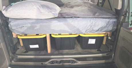 Custom vehicle camping bed with under-bed storage using three yellow-lidded bins. A clever RV rental alternative for road trips.