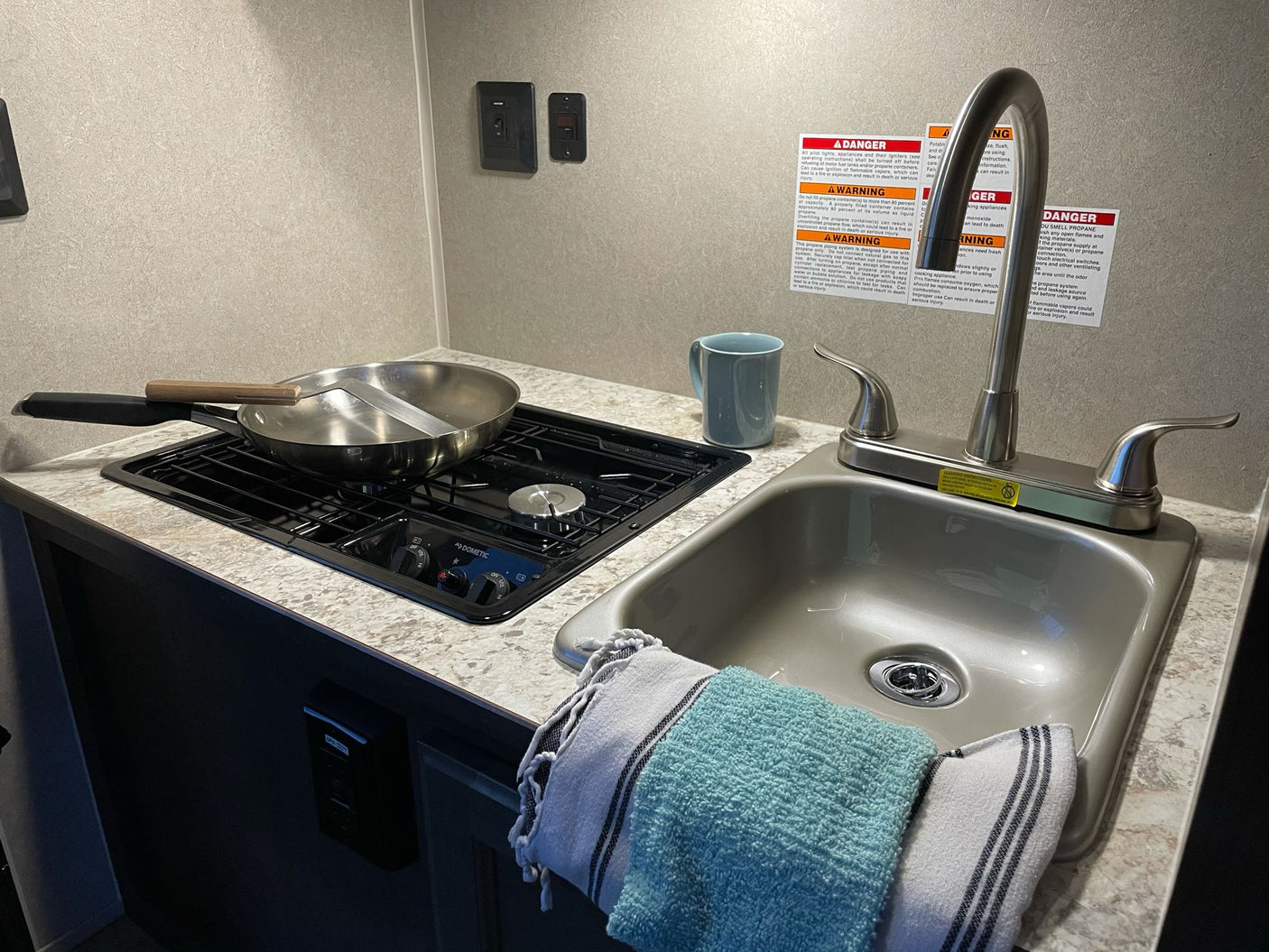 Compact RV rental kitchen featuring a two-burner cooktop, sink, and towels. Ideal for preparing meals on the road.
