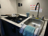 Compact RV rental kitchen featuring a two-burner cooktop, sink, and towels. Ideal for preparing meals on the road.