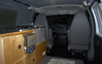 Inside a campervan: custom kitchen with stove, portable heater, fridge, and front seats. Perfect for rv rental! — photo 3
