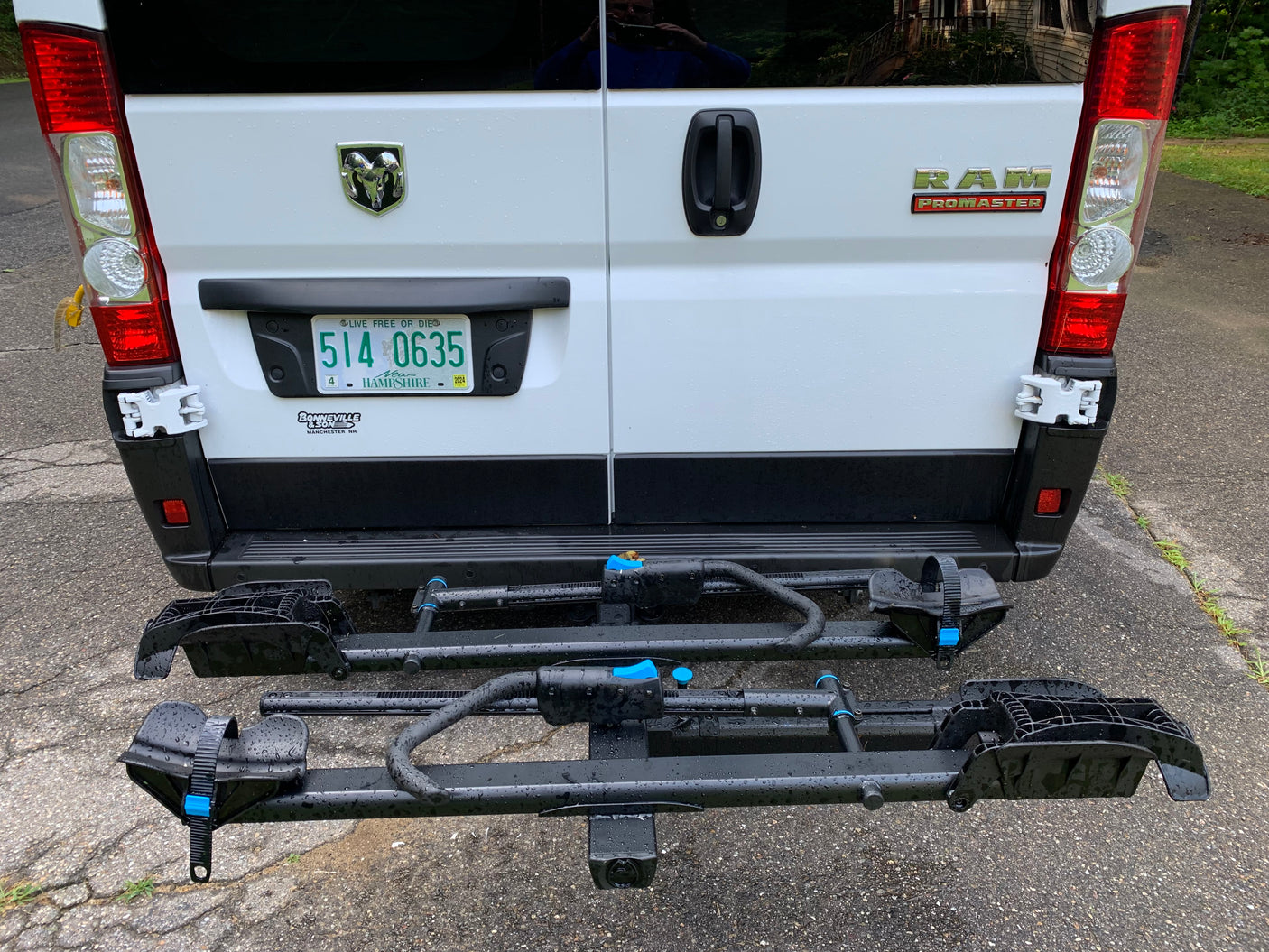 RV rental: Rear of a white Ram ProMaster van with a two-tier bicycle hitch rack, ready for adventure on a wet day.