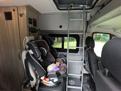 RV rental interior showing multiple child car seats and a ladder to an overhead bunk bed, ready for family travel.