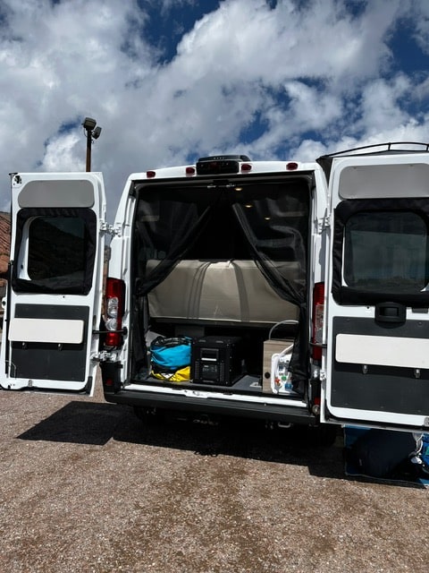  cabinets. Front passenger seat & outdoor view visible.|Step inside this cozy RV rental with a fully equipped kitchen and comfortable living area for memorable travels.|RV rental interior: Camper van's passenger area featuring two white quilted seats — photo 10